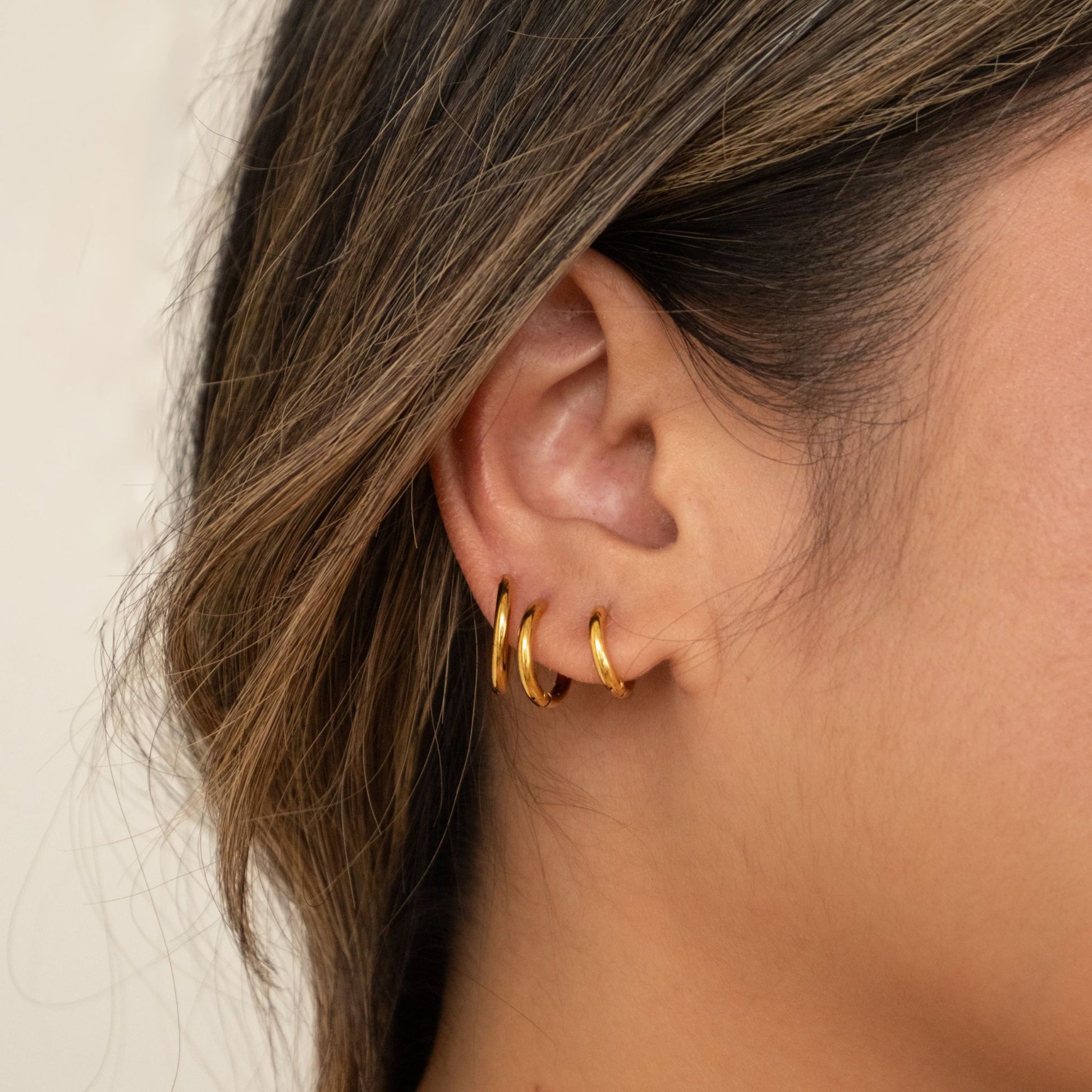 Close-up of an ear wearing mini trio gold hoop earrings 